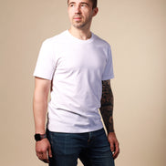 Man wearing a white t-shirt and dark jeans against a beige background