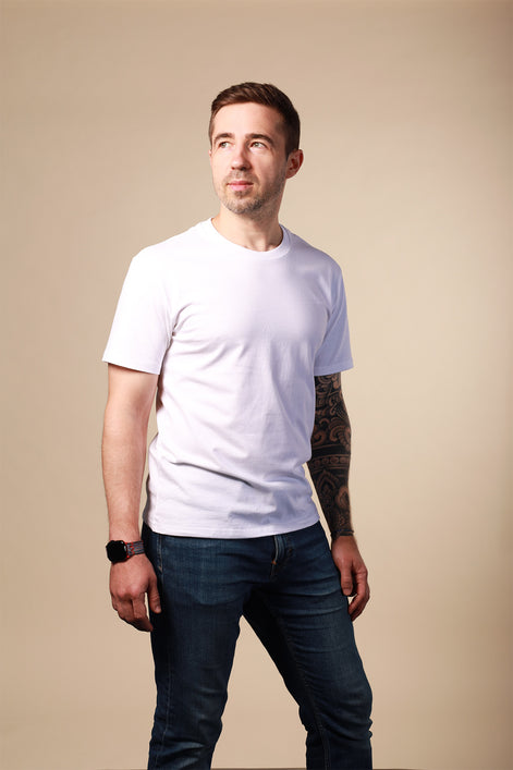 Man wearing a white t-shirt and dark jeans against a beige background