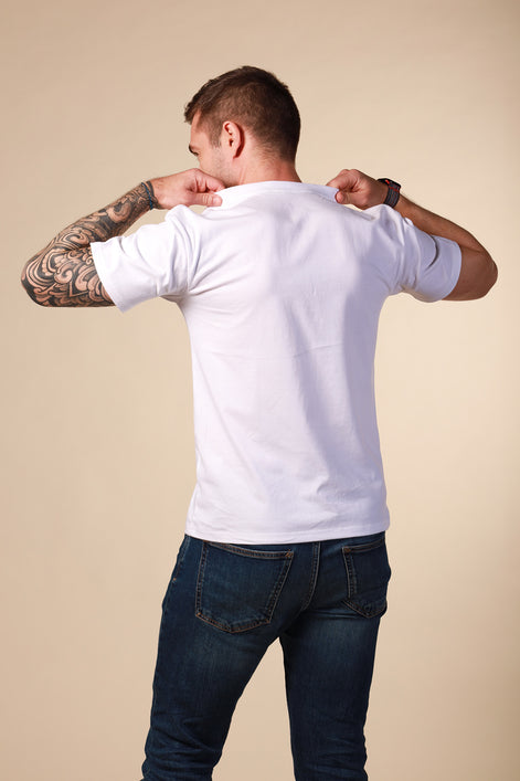 Man wearing a white t-shirt and dark jeans against a beige background