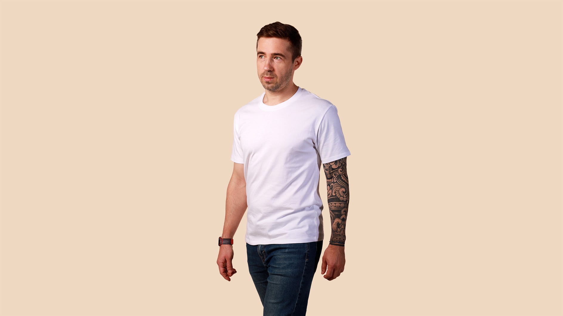 Man wearing a plain white t-shirt and dark jeans on a beige background
