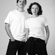 Two people wearing white t-shirts and dark pants against a plain background