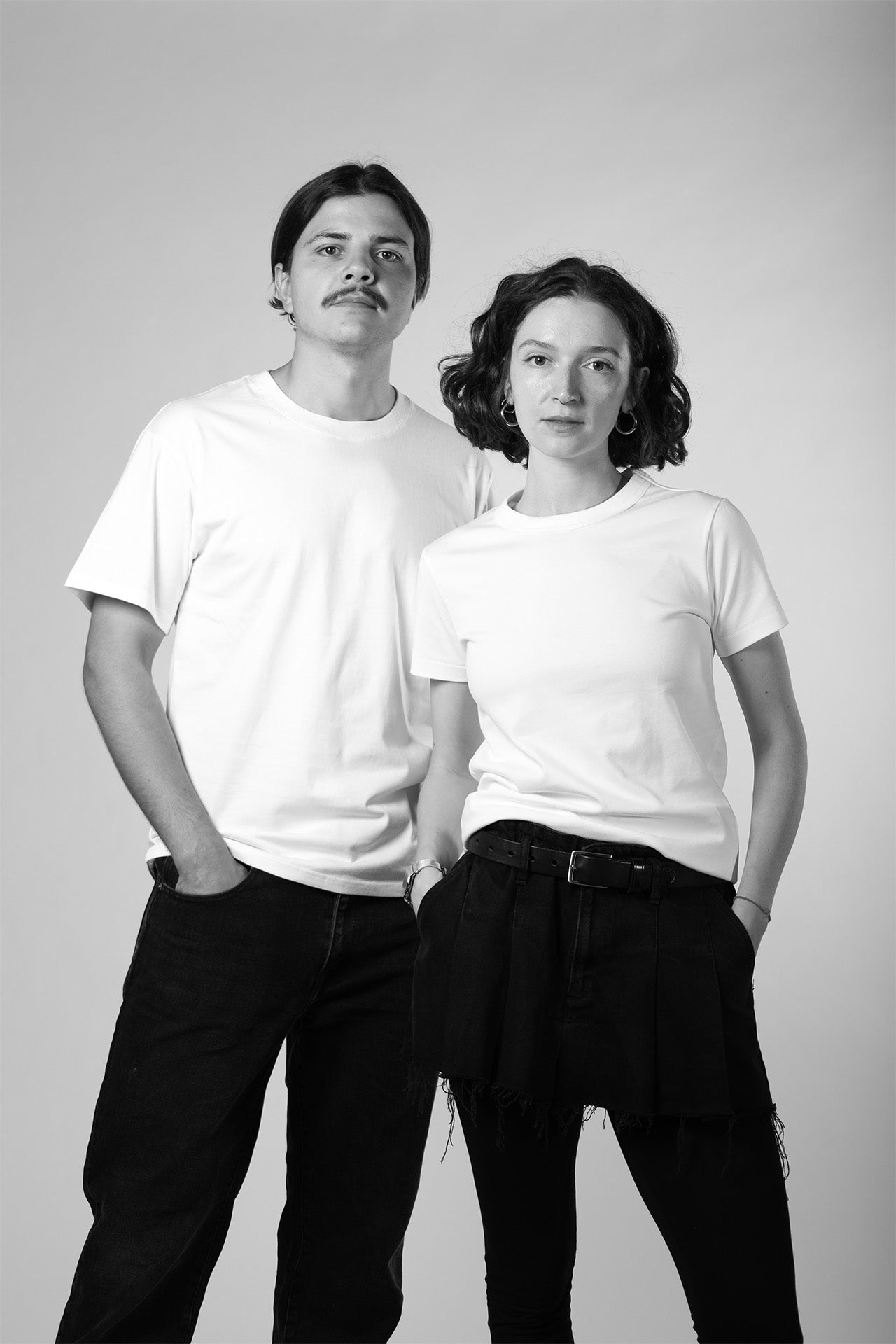 Two people wearing white t-shirts and dark pants against a plain background