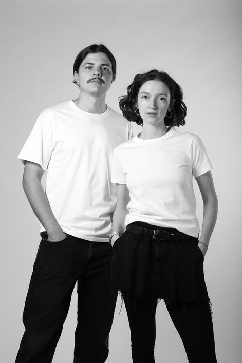 Two people wearing white t-shirts and dark pants against a plain background