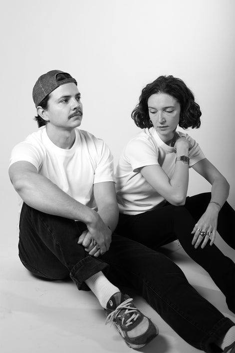 Two people sitting closely together on a plain background