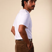 Man wearing a white t-shirt and brown pants against a beige background