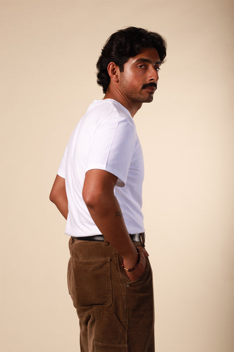 Man wearing a white t-shirt and brown pants against a beige background