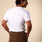 Man wearing a white t-shirt and brown pants against a beige background