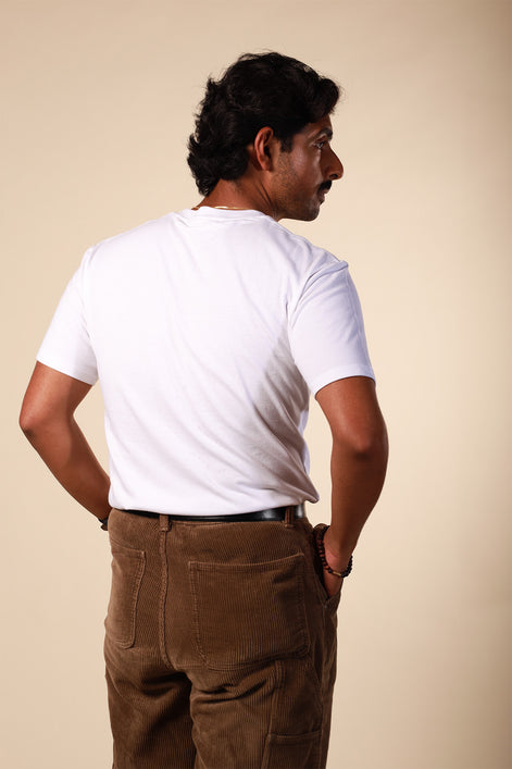 Man wearing a white t-shirt and brown pants against a beige background
