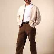 Man wearing a beige jacket, white shirt, and brown pants against a beige background
