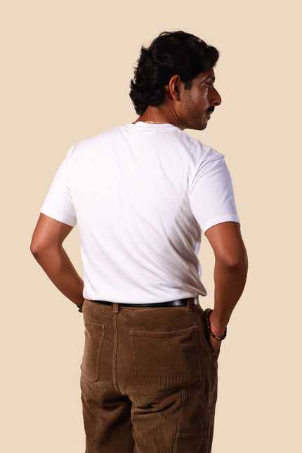 Man wearing a white t-shirt and brown pants against a beige background