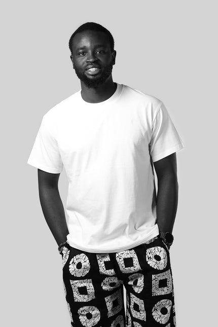 Man wearing a white t-shirt and black pants with geometric pattern on a gray background