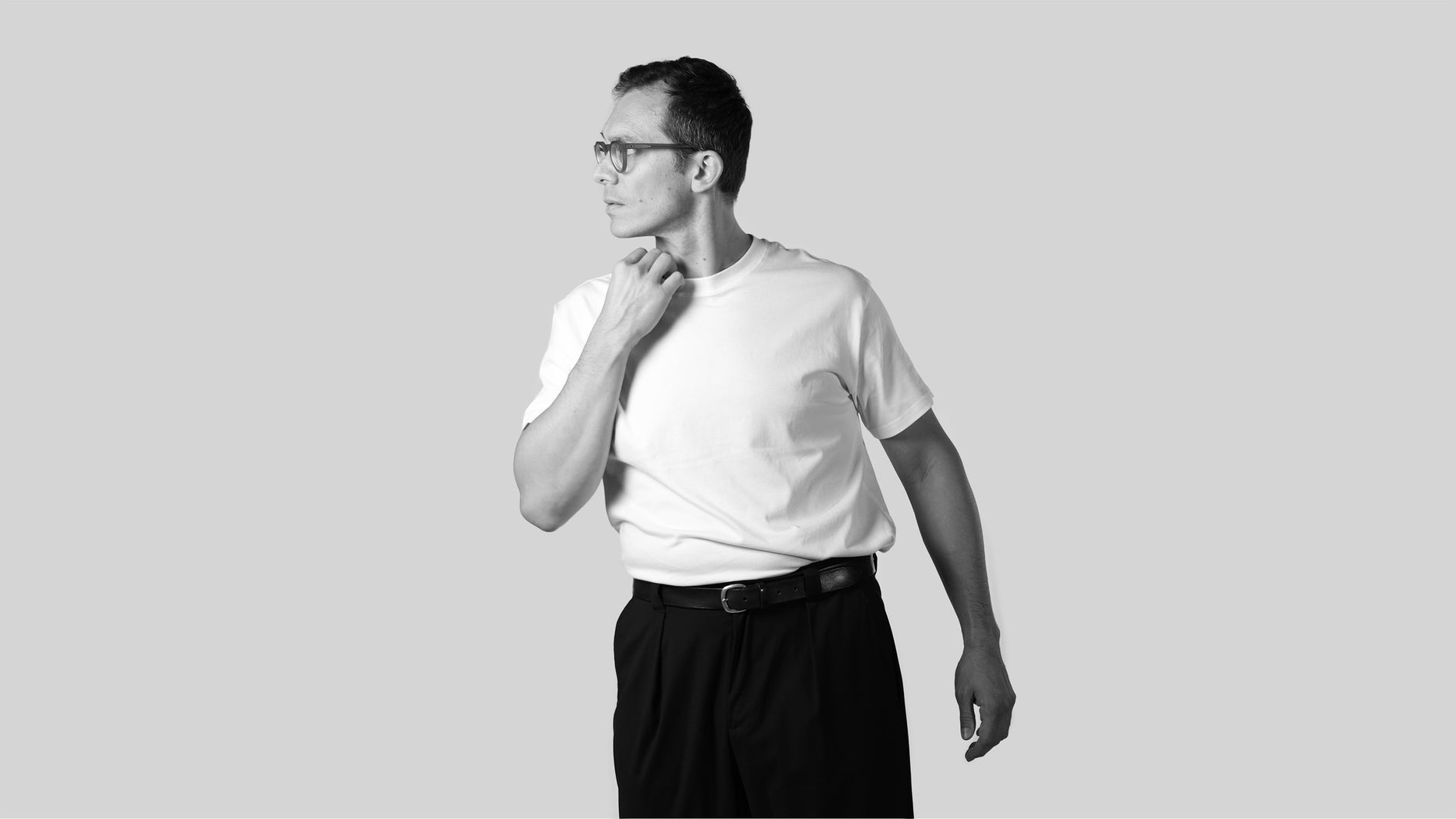 Black and white photo of a person wearing a white t-shirt and dark pants on a light gray background