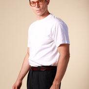 Man wearing a white t-shirt and dark pants against a beige background