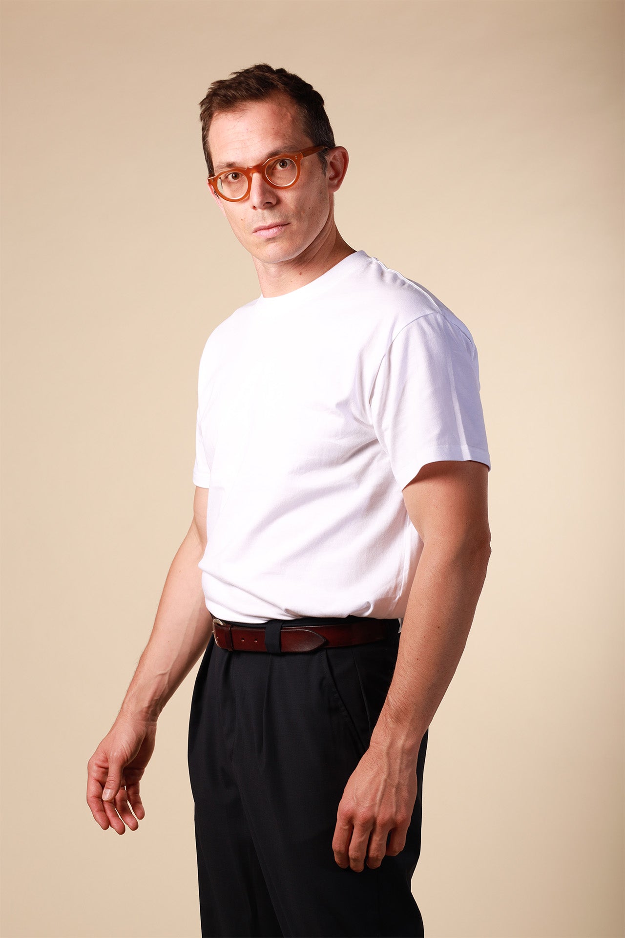 Man wearing a white t-shirt and dark pants against a beige background