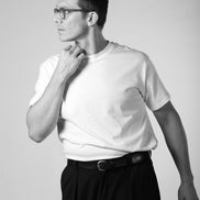 Man wearing a white t-shirt and black pants against a plain background