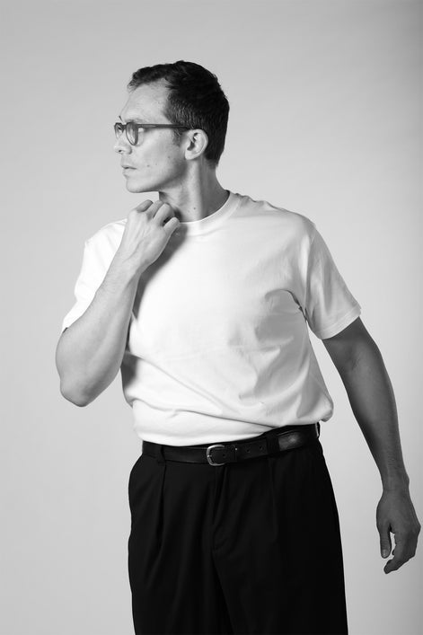 Man wearing a white t-shirt and black pants against a plain background