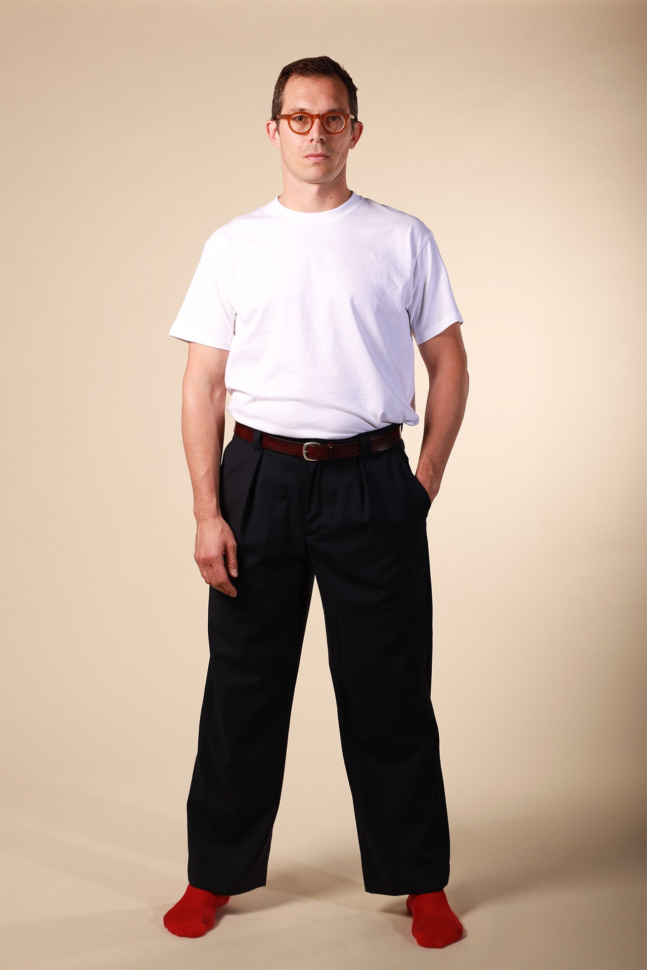 Man wearing a white t-shirt, black pants, and red shoes on a beige background