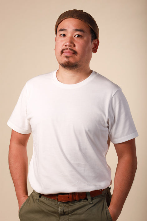 Man wearing a white t-shirt and brown cap against a beige background