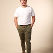 Man wearing a white t-shirt, green pants, and brown shoes on a beige background