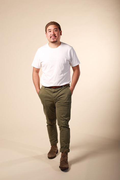Man wearing a white t-shirt, green pants, and brown shoes on a beige background