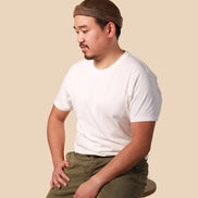 Man wearing a white t-shirt and green pants with a brown headband against a beige background