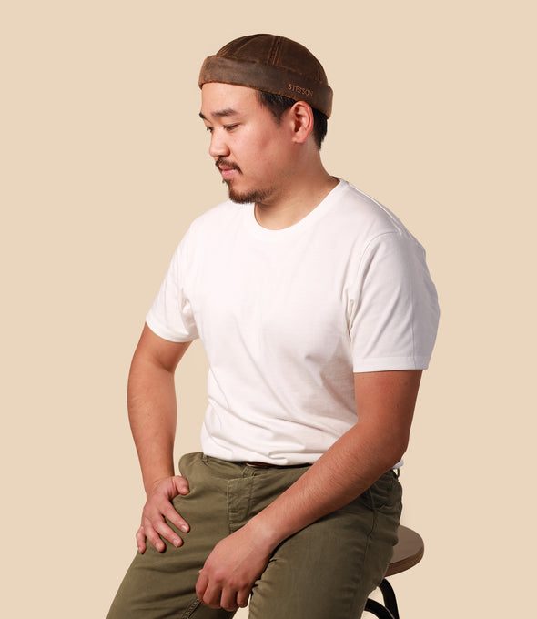 Man wearing a white t-shirt and green pants with a brown headband against a beige background